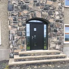 A sleek dark door framed by a stone archway, leading up to a stone step entrance