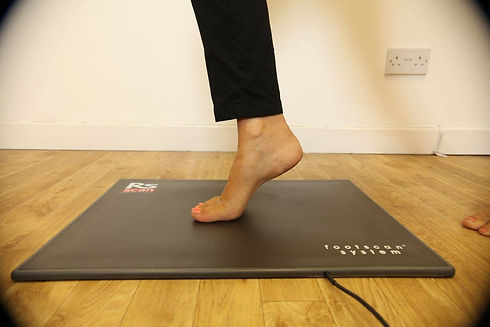 Side view of a person standing bare-toed on one foot atop an electronic pressure analysis machine