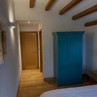 Bedroom with wooden beams, teal wardrobe, white bedding, and wooden door