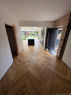 Empty room featuring newly installed herringbone parquet wood flooring leading to an open doorway