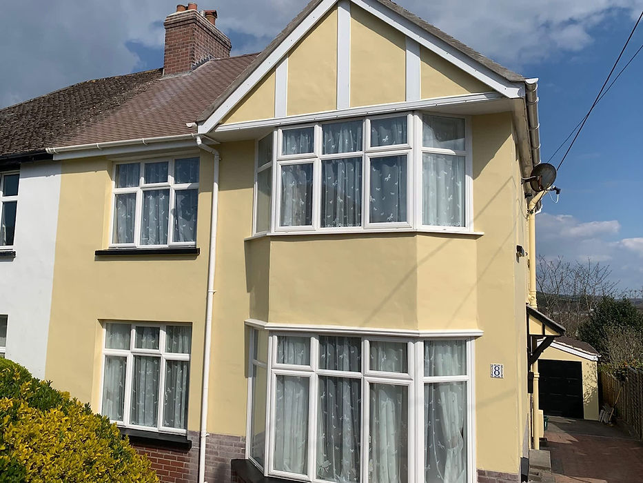 A two-story semi-detached house with yellow and white facade and large bay windows, set under a cloudy sky