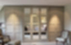 Bespoke classic grey panelled fitted wardrobe wall with integrated central mirror panels in a home setting