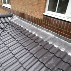 Close-up of a tiled roof edge with a shiny metal flashing, adjacent to a brick wall and window