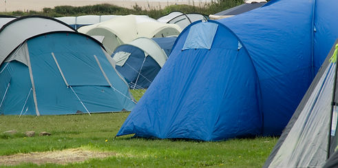 Multiple blue grey and cream tents pitched close together on a grassy campsite ground field outdoors