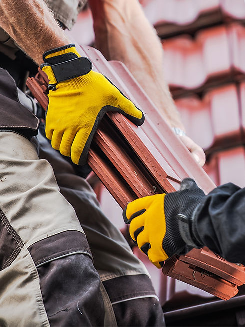 Close-up of two construction workers in yellow gloves passing terracotta roofing tiles