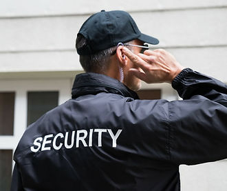 Security guard in a black uniform and cap with "SECURITY" on the back, holding an earpiece