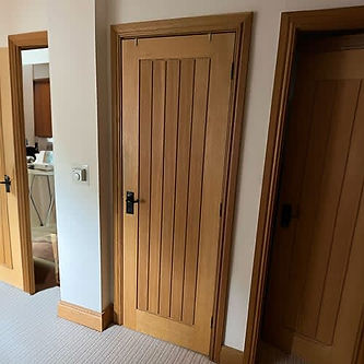 A wooden door with vertical panels and a black handle, set in a light-coloured hallway