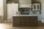 A kitchen with a brown island, two glass pendant lights, a bar stool, and wooden cabinets
