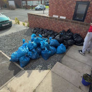 Pile of blue and black garbage bags on gravel beside a brick wall