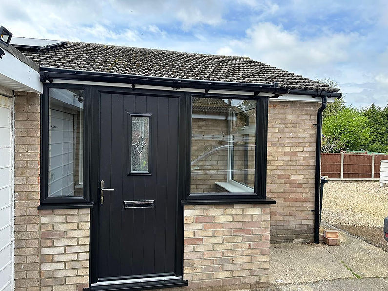 A modern, black front door with a decorative glass panel, set in a small brick porch