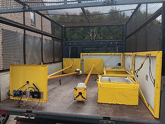 A truck bed with a wire mesh cage contains dismantled yellow metal barriers