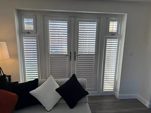 A room featuring white plantation shutters on French doors flanked by smaller windows
