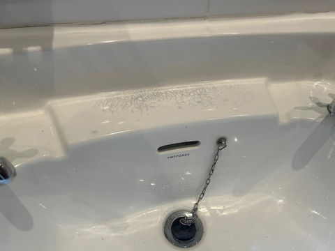 A broken white bathtub and a chain-linked drain stopper