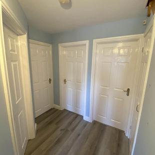 A small hallway with light blue walls features three closed white doors with brass handles