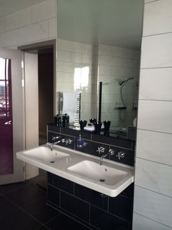 A bathroom with a double sink, a large mirror, sleek black and white tiles, and a glass shower