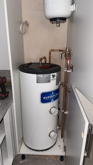 A compact utility space features a white cylindrical boiler with copper pipes and valves