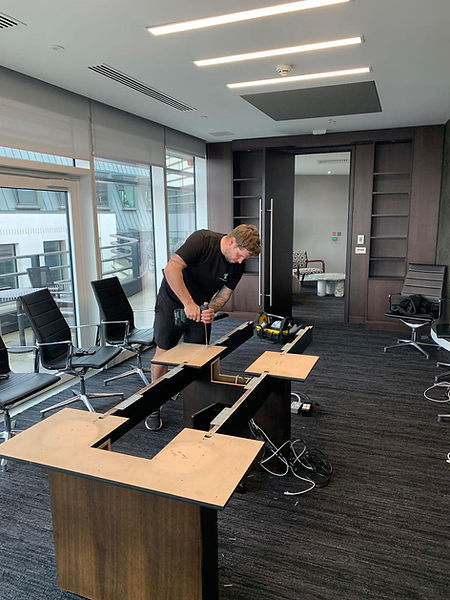 Man assembling furniture in an office with large windows and empty, modern chairs