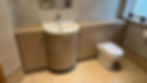 A bathroom featuring a wooden vanity with a circular sink, a white toilet, and stylish beige tile flooring