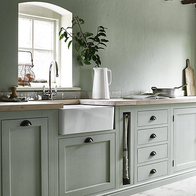 A kitchen with pastel green cabinets, wooden countertops, and a farmhouse sink