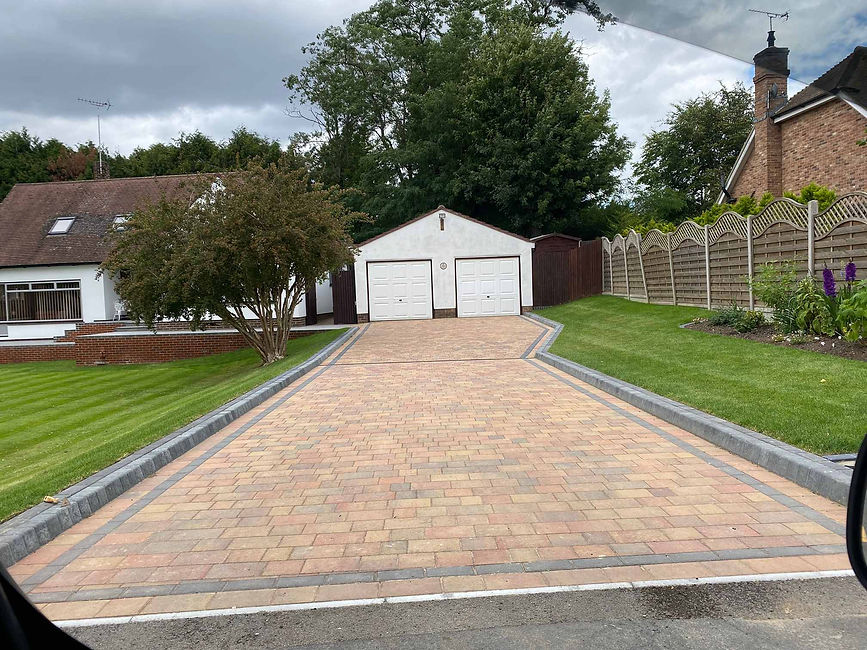 A well-maintained driveway with brick paving leads to a white garage