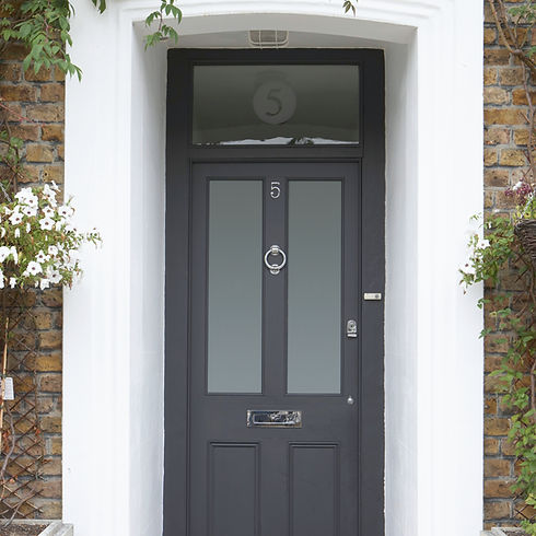 A black front door with a silver knocker and mail slot, flanked by white columns and climbing plants
