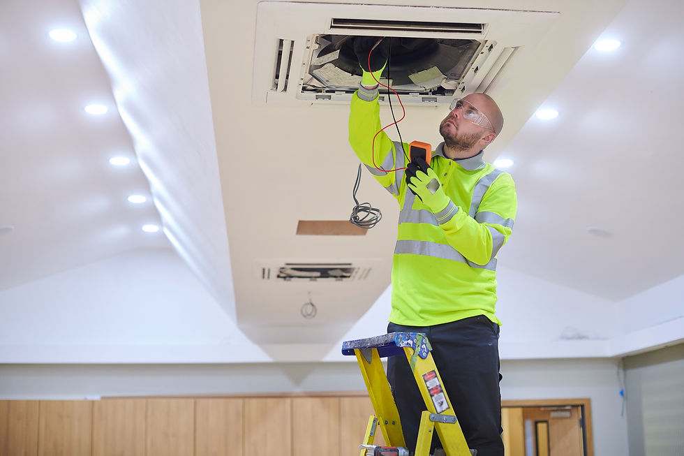 A technician in a high-visibility shirt and safety glasses repairs a ceiling HVAC unit with a multimeter