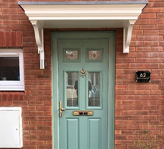 A green door with decorative glass panels set in a red brick wall