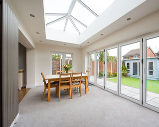 Bright home extension dining area featuring a large glass roof lantern and white bi-fold doors