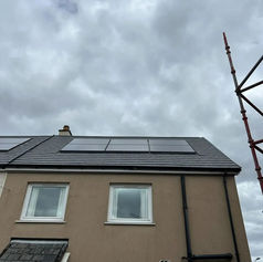 Black solar panels on a dark tiled roof of a tan house with scaffolding against a cloudy sky
