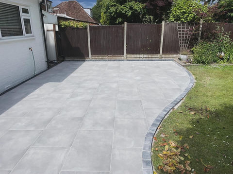 Newly laid grey patio tiles with curved edges next to a green lawn