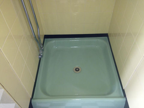 A green square shower base with a glass enclosure and yellow tiles