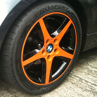 A BMW wheel with a sleek black finish and vibrant orange accents