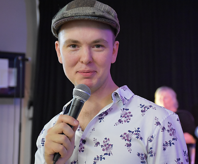 Matthew Harriage holding a microphone and wearing a hat and floral shirt
