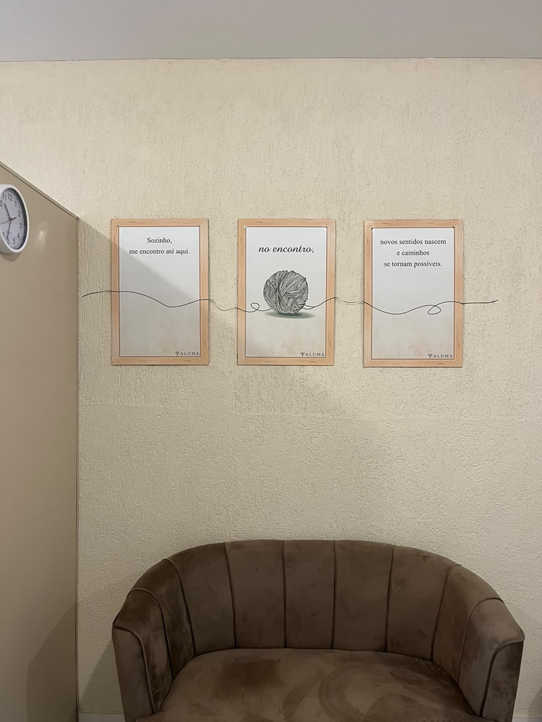 Foto da parede da Clínica Aluma com três quadros alinhados e um sofá bege abaixo, em ambiente clean e acolhedor, com foco nos quadros.