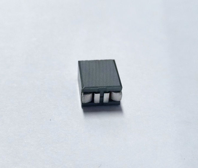 Small electronic component with three pins on a shiny gray surface.