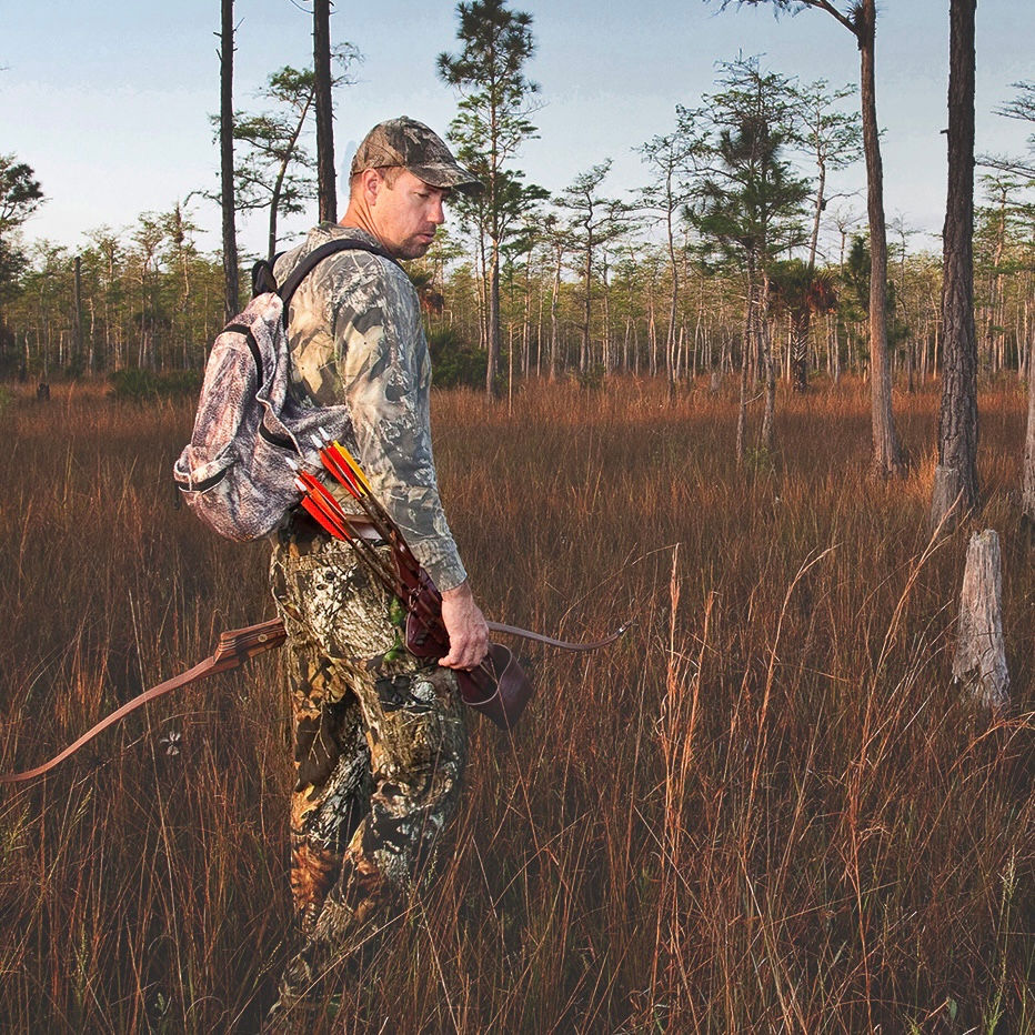 David is dressed in full camoflauge and is stalking through the bush in central Florida. He is carrying his brightly colored arrows and a recurve bow. 