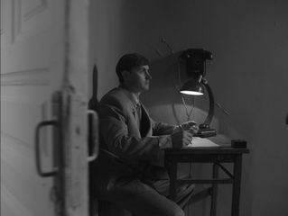 Man in suit writing at desk, lamp illuminating vintage telephone.