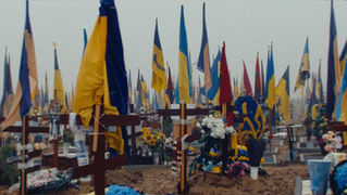 Cemetery with graves marked by crosses and Ukrainian flags.