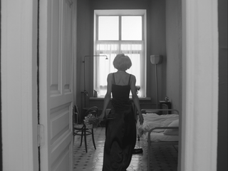 Woman in long dark dress entering an old hospital room, black and white.