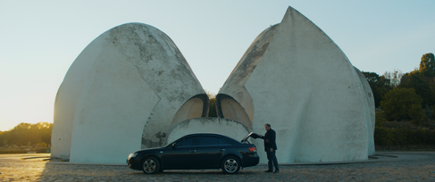 Man opens dark car's trunk by two large white shell structures.