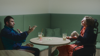 Man gesturing, talking to woman in wheelchair at cafe booth.