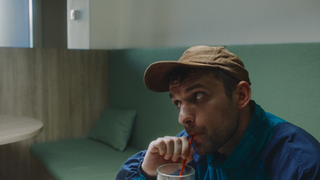 Man in brown cap sips drink with red straw in modern booth.