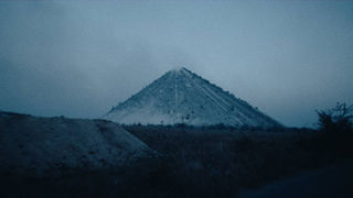 Dark, pyramid-shaped mound under an overcast sky