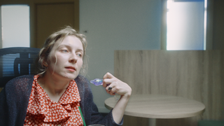 Blonde woman in red shirt holding planet charm, looking thoughtfully indoors.