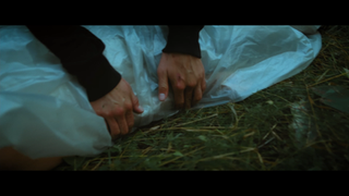 Woman's hands manipulating white plastic sheet on dark grass. Dystopia Feature Film.