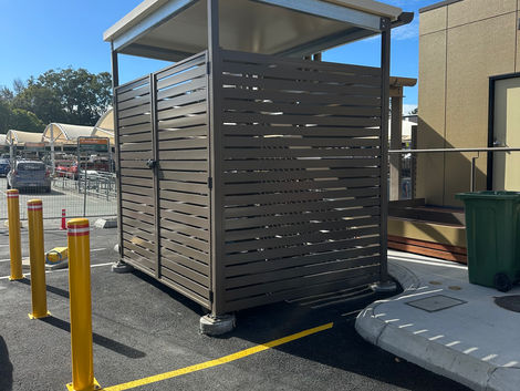 Roofed aluminium slat bin enclosure at a commercial site.