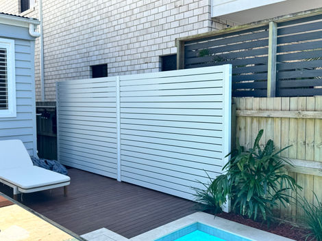 White aluminium slat privacy screen beside a pool deck, shielding the area from view.