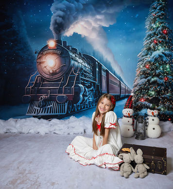 Child posing by Christmas train and decorated tree in winter studio.