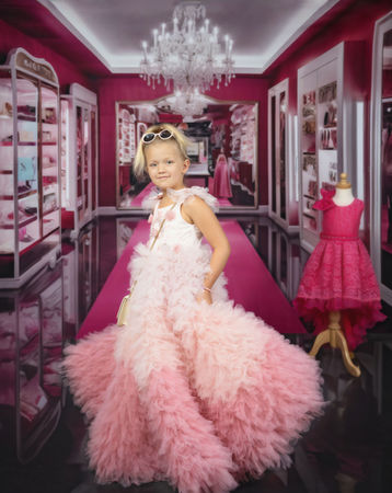 Young girl in a pink Barbie-style ruffled gown posing in a glamorous fashion boutique setting during a Barbie-inspired photo session.
