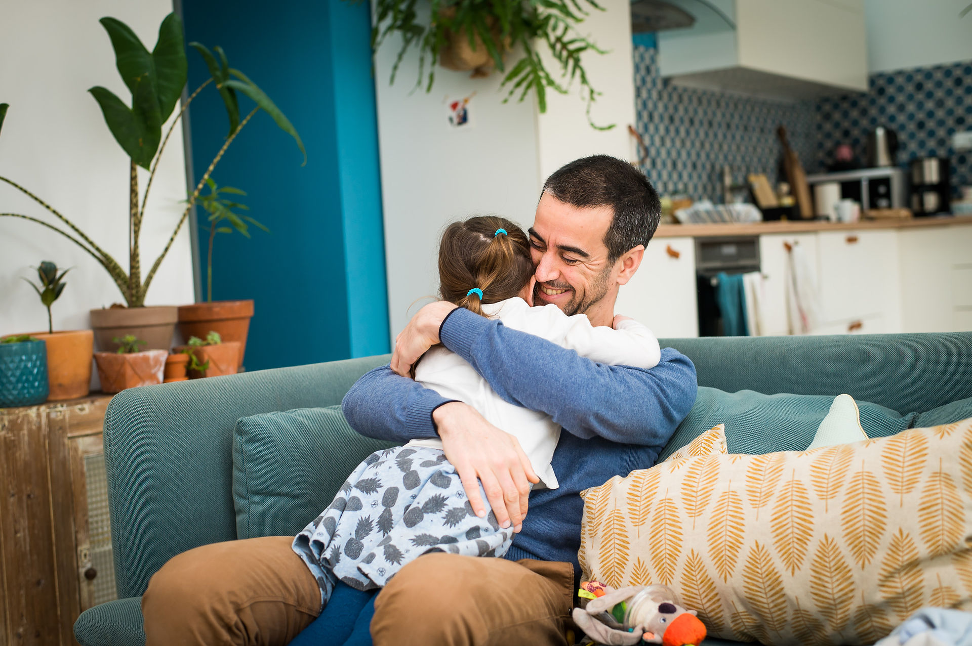 Petite fille faisant un câlin tendre à son papa sur le canapé lors d'une séance photo famille à domicile à Nantes